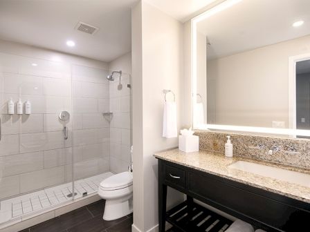 Modern bathroom with a glass shower, toilet, and granite-topped vanity, featuring clean lines and a minimalist design.