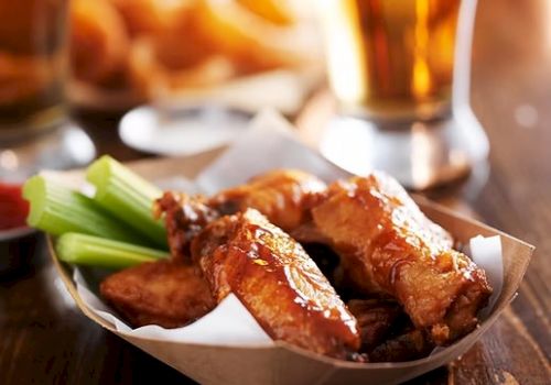 Plate of crispy fried chicken wings with celery sticks, dipping sauce, and a beer in the background.