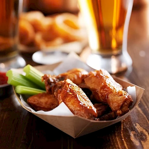 Plate of crispy fried chicken wings with celery sticks, dipping sauce, and a beer in the background.